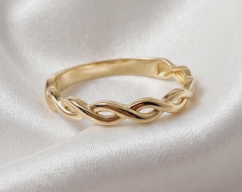May include: A polished gold ring featuring a continuous twisted rope or braided metal design. The band has a smooth, reflective surface with a repeating interlocking pattern that creates a series of small, uniform open loops.