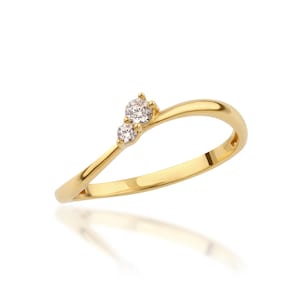 May include: A gold ring featuring two clear, round gemstones. The ring has a curved design, with the gemstones set on the upper curve. The ring is displayed on a white background, with a reflection visible below.