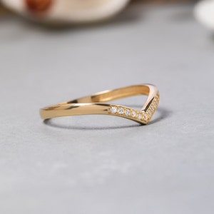 May include: A gold band ring with a V-shaped design and small clear stones set along the top edge.