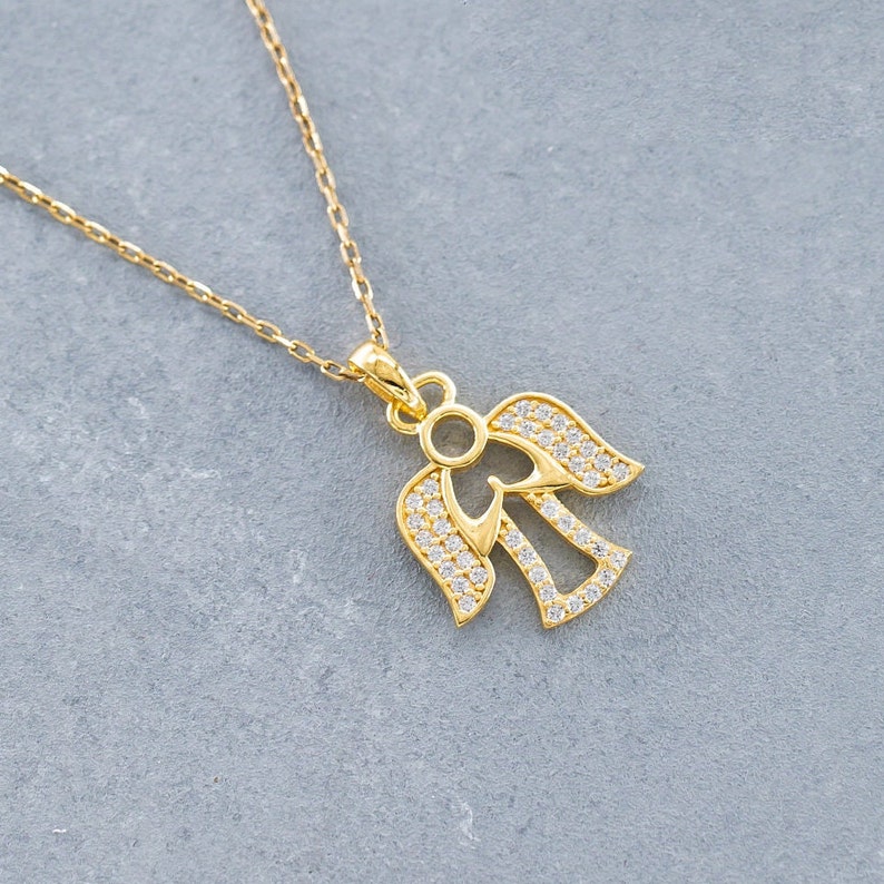 K&ouml;nnte beinhalten: Eine goldene Halskette mit einem klaren Kristall-Engel-Anh&auml;nger. Der Engel hat einen Heiligenschein und ausgebreitete Fl&uuml;gel.