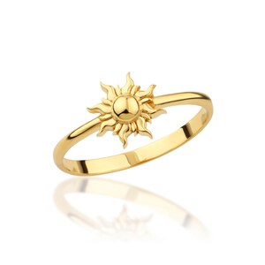May include: A gold ring with a sun design. The sun is detailed with rays and a round center.