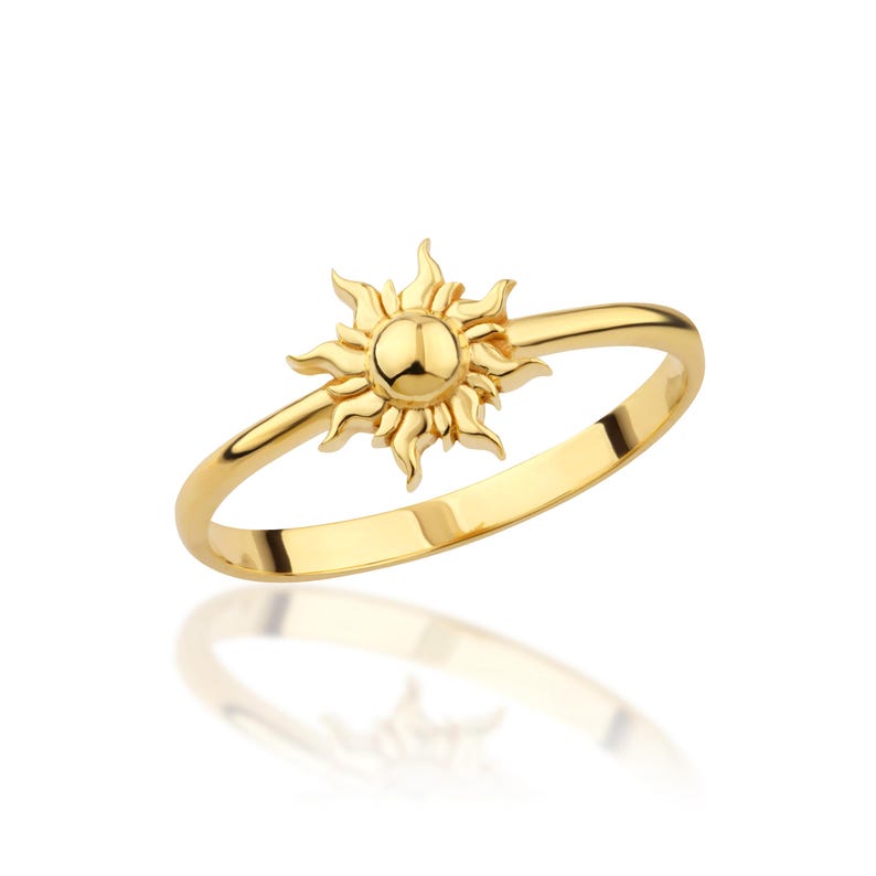 May include: A gold ring with a sun design. The sun is detailed with rays and a round center.