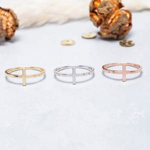 May include: Three simple gold, silver, and rose gold rings with a cross design. The rings are on a white surface.