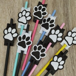 May include: Nine black and white paw print designs on colorful straws. The straws are pink, blue, black, and turquoise. The paw prints are all the same size and shape, but they are arranged in different directions.