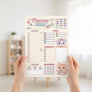 May include: A cream-colored 2026 planner with a cute cat theme. The planner includes sections for scheduling, to-do lists, shopping lists, and notes. It features a monthly calendar, nutrition tracker, and water tracker. The planner is held by two hands.