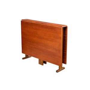 May include: A folded, rectangular wooden table with a warm, reddish-brown finish. The table has a simple design with two supporting legs. The table is likely made of solid wood and is suitable for small spaces.