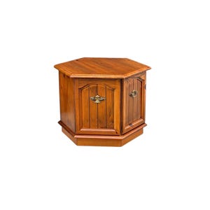 May include: A hexagonal wooden side table with a warm brown finish. The table features two cabinet doors with brass-colored handles and vertical paneling. The top is also hexagonal. A decorative piece of furniture.
