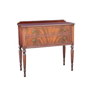 May include: A dark brown wooden console table featuring two horizontal drawers with decorative fan-patterned wood grain veneers. The piece includes a low back gallery, fluted side columns, and four slender, turned legs with brass hardware pulls.