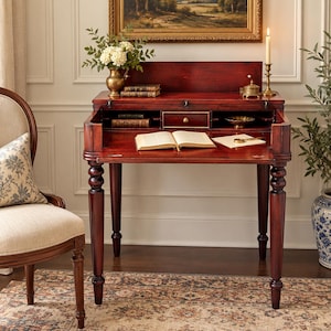 May include: A dark cherry wood secretary desk featuring a drop-down writing surface, a central drawer with a brass knob, and open storage compartments. The desk stands on four turned legs and includes a hinged top section that folds upward.