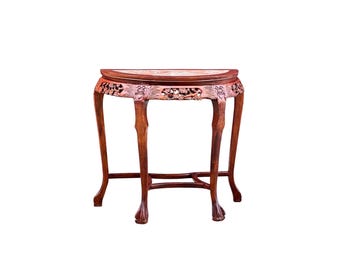 May include: A semi-circular wooden console table with a reddish-brown finish. The apron features intricate floral carvings, and the four curved legs terminate in claw-and-ball feet, connected by a central cross-stretcher support structure.