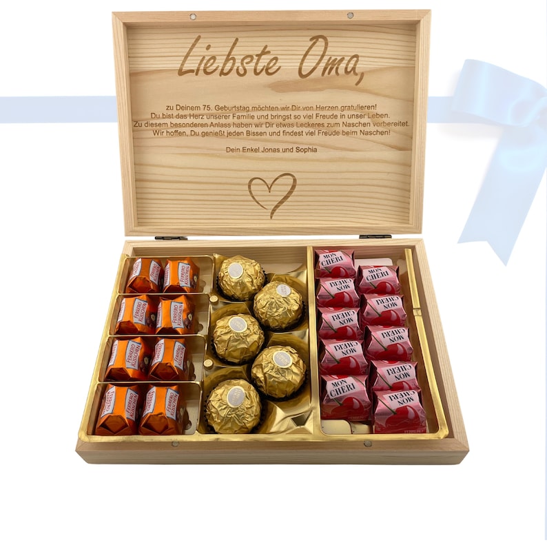 Op de afbeelding: Een houten doos met een hartvormig ontwerp op de deksel. De deksel is open en de doos is gevuld met verschillende chocolaatjes. De chocolaatjes zijn in twee rijen gerangschikt, waarbij de bovenste rij een selectie chocolaatjes bevat en de onderste rij een selectie chocolaatjes bevat. De doos is voorzien van de tekst "Liebste Oma" en een bericht waarin de ontvanger gefeliciteerd wordt met haar 75e verjaardag.