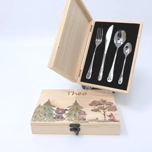 Könnte beinhalten: Ein Kinderbesteck-Set aus Holz, bestehend aus Gabel, Messer und zwei Löffeln. Die Box ist mit einer Waldszene und dem Namen "Theo" verziert. Jedes Besteckteil ist mit dem Namen "Theo" graviert.