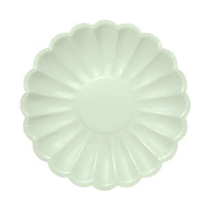Puede incluir: Un plato de papel verde pálido con un borde festoneado decorativo. El plato tiene un centro circular y líneas radiales que se extienden hasta el borde, dándole un aspecto texturizado en forma de flor. El plato está sobre un fondo blanco.