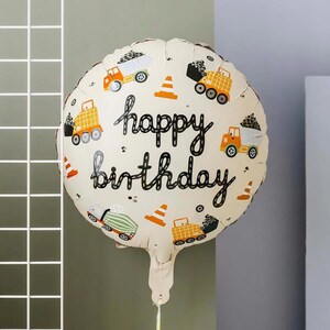 Puede incluir: Globo de cumpleaños redondo color crema con la frase "happy birthday" en escritura negra. El globo está decorado con camiones de construcción naranjas, conos de tráfico y puntos negros. El globo está inflado y listo para una celebración.