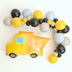 Puede incluir: Un globo de camión volquete amarillo con ruedas negras y una guirnalda de globos grises, negros y amarillos.