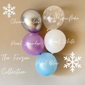 Puede incluir: Una colección de seis globos en varios colores y acabados. Los globos incluyen plata cromada, lavanda nacarada, blanco nacarado, azul nacarado y un globo transparente con copos de nieve. El texto "The Frozen Collection" está escrito debajo de los globos.
