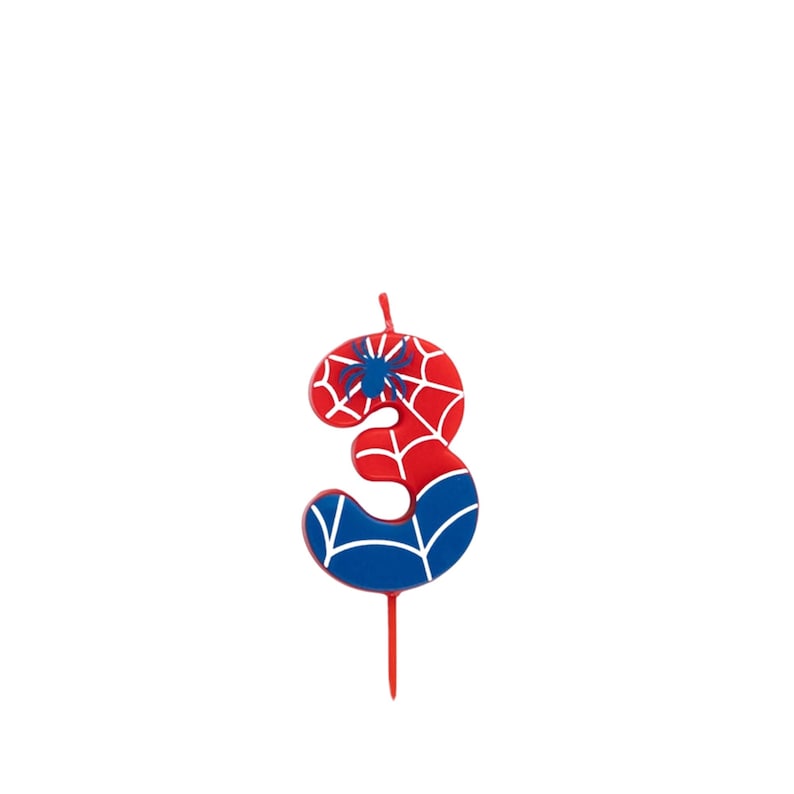 May include: A number three birthday candle in red, white, and blue, featuring a spiderweb design and a blue spider. The candle is designed with a red stem and is suitable for a birthday celebration.