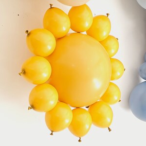 May include: A yellow balloon sun decoration with a large yellow balloon in the center and smaller yellow balloons surrounding it.