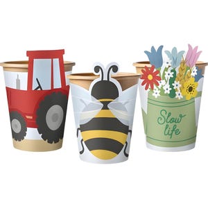 Puede incluir: Tres vasos de papel con diseños de temática agrícola. Un vaso presenta un tractor rojo, otro una abeja de dibujos animados y el tercero un cubo verde con flores y la frase "Slow life".