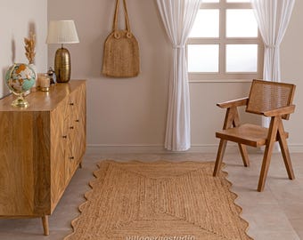 Könnte beinhalten: Ein rechteckiger Jute-Teppich mit gewelltem Rand wird auf einem gefliesten Boden gezeigt. Der Teppich hat ein geometrisches Design in der Mitte. Eine Holzkommode, ein Globus, eine Lampe und eine gewebte Tragetasche sind ebenfalls im Raum zu sehen. Der Text "villagerugstudio" befindet sich am unteren Rand des Teppichs.