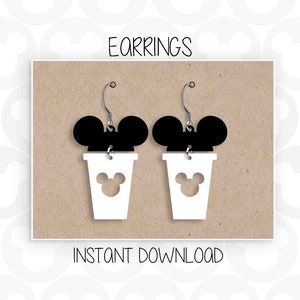 Puede incluir: Un par de pendientes de taza de café blanca con una silueta negra de Mickey Mouse en la parte superior. Los pendientes tienen un gancho plateado y una silueta blanca de Mickey Mouse recortada en la parte delantera de la taza.