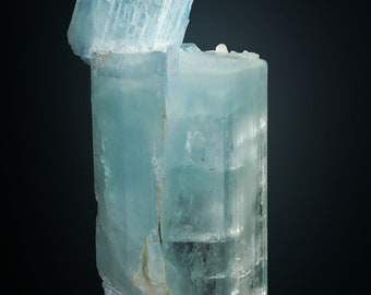 May include: A large, light blue aquamarine crystal with a clear, glassy texture. The crystal is faceted and has a sharp, pointed tip. It is a beautiful example of this gemstone.