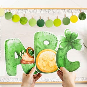 May include: Green ABC letters with St. Patrick's Day decorations. The letter A features a cupcake and cookie, the letter B has a gold coin, and the letter C is a shamrock. A garland of green circles hangs above the letters.