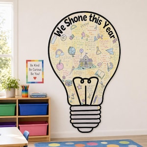May include: A large lightbulb-shaped wall decal featuring the text "We Shone this Year" and various hand-drawn illustrations including a schoolhouse, globe, apple, and books, alongside a separate rectangular poster with the text "Be Kind Be Curious Be You!"