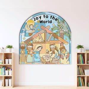 May include: A large, arched wall decal featuring a colorful nativity scene illustration with the text "Joy to the World" at the top. The design depicts an angel, a stable, and figures surrounding a manger, rendered in a stained-glass style.