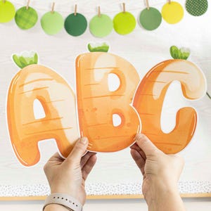 Pode incluir: Três letras laranja em forma de cenoura, A, B e C, com topos verdes. As letras estão sobre um fundo branco com um padrão xadrez verde e branco.