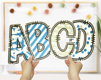 May include: Four large cardboard letters, A, B, C, and D, are held in front of a white background. The letters are decorated with different blue and white patterns, including stripes, polka dots, and a shark pattern.