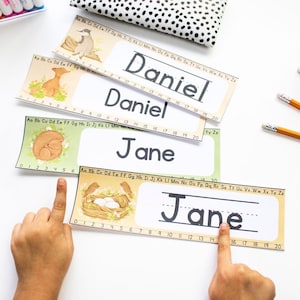 Può includere: Quattro schede di tracciamento dei nomi stampabili con uno sfondo giallo e un'illustrazione colorata su ogni scheda. Le schede presentano i nomi Daniel, Daniel, Jane e Jane. Ogni scheda ha una linea per tracciare il nome e una linea numerica da 0 a 20.