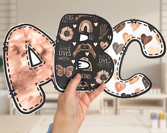 May include: Three large cardboard letters, A, B, and C, with a brown and black patterned design. The letters are decorated with hearts, sunflowers, butterflies, and the phrase "Black Lives Matter".