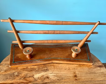 May include: A wooden coat rack with three horizontal bars and two hooks. The rack has a green trim and is made of light brown wood.