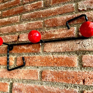 Puede incluir: Un perchero de metal negro con tres ganchos redondos montados en una pared de ladrillo.