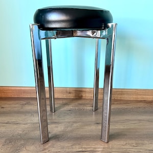 May include: A black leather upholstered stool with a chrome frame. The stool has four legs and a round seat.