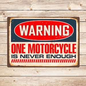 May include: A vintage-style metal sign with a red warning sign that says "WARNING" in white letters. The sign has a white background with blue borders and says "ONE MOTORCYCLE IS NEVER ENOUGH" in black letters with red stripes at the bottom.