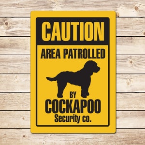May include: Yellow caution sign with black text and a silhouette of a Cockapoo dog. The sign reads "Caution Area Patrolled by Cockapoo Security Co."
