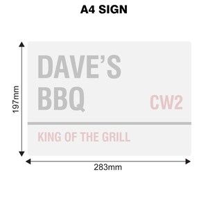 May include: A white A4 sign with gray text that reads "Dave's BBQ King of the Grill" and "CW2" in pink text. The sign measures 11.7 inches by 11.1 inches.