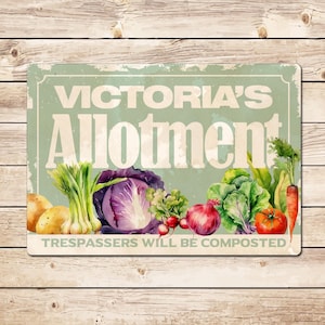 May include: A rectangular sign with the text "Victoria's Allotment" in white letters on a light green background. The sign features illustrations of various vegetables, including potatoes, cabbage, and tomatoes. The text "Trespassers Will Be Composted" is at the bottom.
