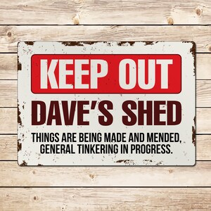 May include: A white metal sign with a red border and the text "KEEP OUT DAVE'S SHED THINGS ARE BEING MADE AND MENDED, GENERAL TINKERING IN PROGRESS."