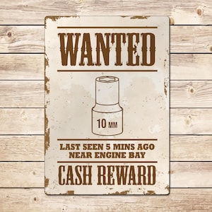 May include: A vintage-style metal sign with a distressed, rusty look. The sign reads "WANTED" in large, brown letters. A line drawing of a 10 mm socket wrench is shown below the text. The sign also reads "Last seen 5 mins ago near engine bay. CASH REWARD."
