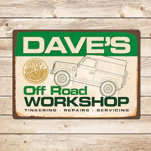 May include: A green and brown metal sign with the text "Dave's Off Road Workshop" and the words "Tinkering, Repairs, Servicing". The sign features a cartoon image of a Land Rover.