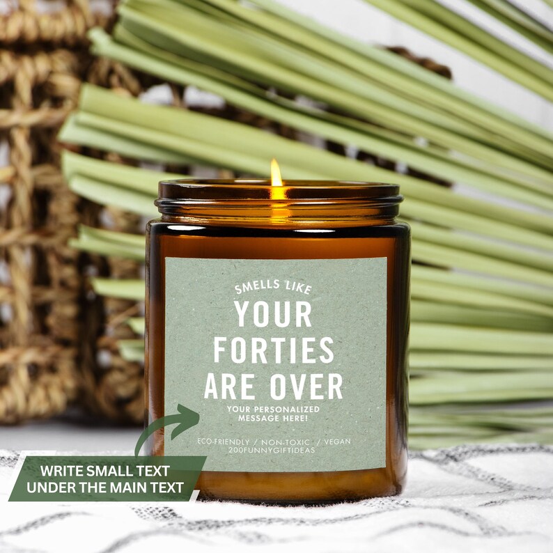 May include: A brown glass candle jar with a green label that reads "Smells like your forties are over. Your personalized message here! Eco-friendly/Non-toxic/Vegan 200funnygiftideas".
