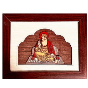 May include: A framed artwork featuring a religious figure with a long white beard, wearing a red robe and turban. The figure is seated on a patterned rug against a wood-grain background, framed in dark brown. The artwork is set within a white border.