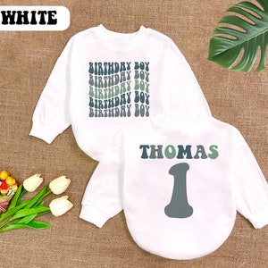 May include: White long-sleeved sweatshirt with the text "Birthday Boy" repeated in a retro font in green and black. A second white long-sleeved sweatshirt with the text "Thomas" in a retro font in green and black and the number "1" in gray.