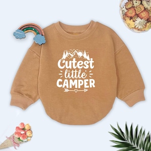 May include: A brown sweatshirt with a white graphic that says "Cutest little camper" with a mountain and tree design.