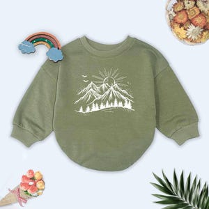 May include: A green long-sleeved sweatshirt with a white mountain range and sun graphic. The sweatshirt has a round neckline and a relaxed fit.