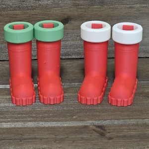 May include: Four red, miniature rain boots with green and white accents. The boots have a textured surface and a scalloped sole. The boots are arranged in two pairs, side-by-side, on a wooden surface.