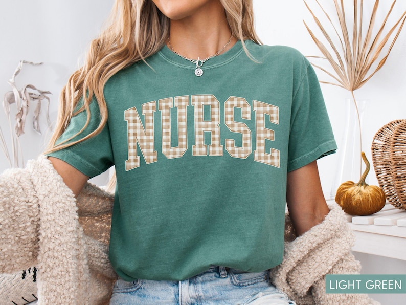 May include: A light green t-shirt with the word "NURSE" in large, tan plaid letters. The shirt has short sleeves and a crew neck. The text "LIGHT GREEN" is at the bottom right corner of the image.